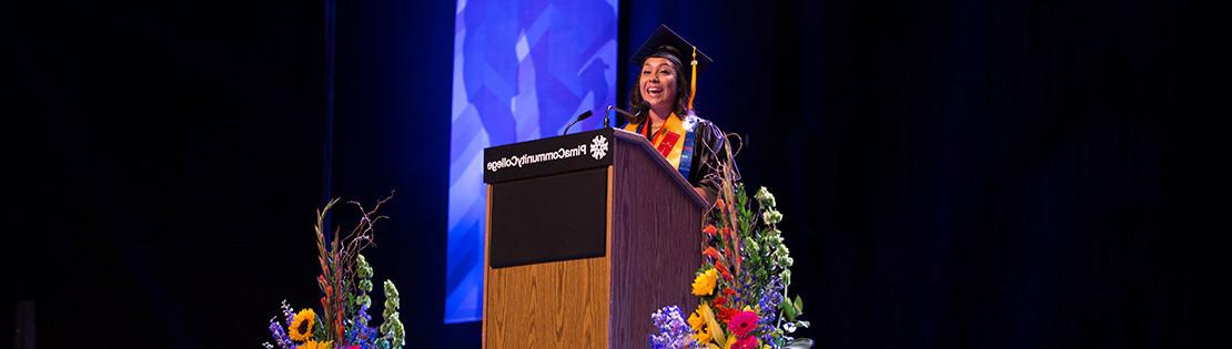 A woman stands speaking at Pima's graduation ceremony