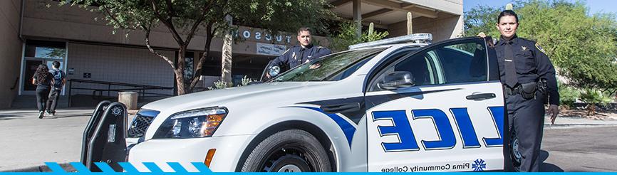 Two campus police stand in front of a squad car